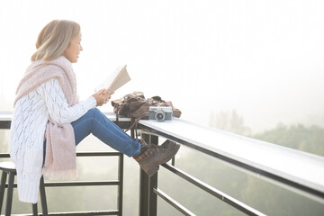 young woman reading book or bible near window and looking mountain view at countryside homestay in the morning sunrise with copy space. journey, trip and relaxing concept. coats blankets in winter.