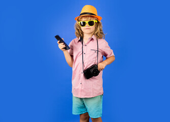 Kid traveller. Child holding mobile phone and camera, traveling photographer. Fashion boy with summer hat, shirt and sunglasses.