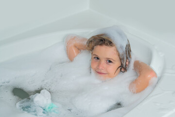 Bath tub with soap bubble. Funny boy with wet curly hair taking a bath in a kitchen sink with lots...