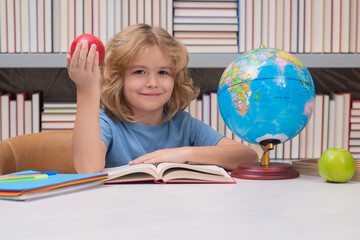 School boy with books and apple in library. School kid looking at globe in library at the elementary school. Child from elementary school. Pupil go study. Clever schoolboy learning.