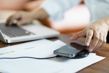 Charging mobile phone battery with wireless charging device in the table. Smartphone charging on a charging pad. Mobile phone near wireless charger Modern lifestyle technology concept