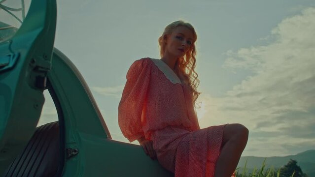 Portrait of a girl in a pink vintage dress sitting on the trunk of a turquoise colored retro car