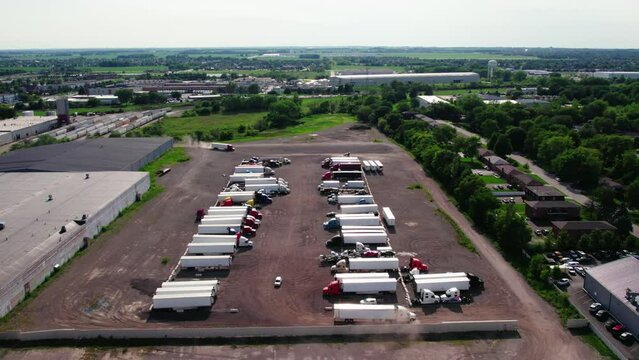 sideways aerial yard parking lot with semi trucks and trailers - reefers, dry van, flatbeds, stingers, bob tails. Truck Driver is backing up. Plainfield Illinois USA