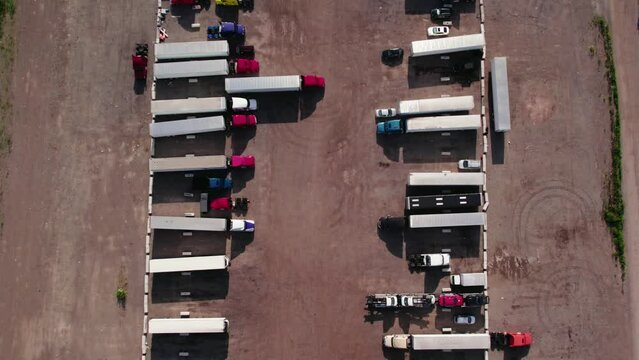 top down aerial of yard parking lot with semi trucks and trailers - reefers, dry van, flatbeds, stingers, bob tails. Truck Driver is backing up. Plainfield Illinois USA