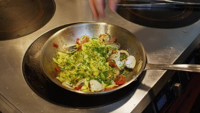 Spaghetti o tagliatelle with seafood preparation in professional restaurant kitchen, chef add green Persley before plate 
