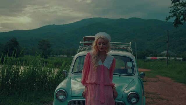 Portrait of a girl in a pink vintage dress sitting on the hood of a turquoise-colored retro car