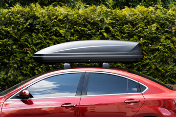 Trunk installed on roof of red sedan car. Equipment for travel. Concept of storage, transportation