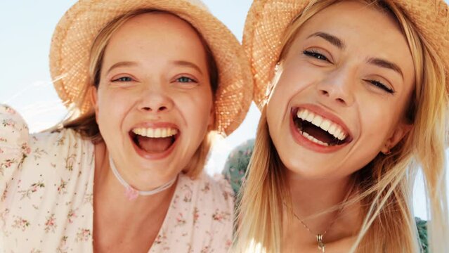 Two young beautiful smiling hipster woman in trendy summer sundress. Carefree women posing in street in hats. Positive models having fun and hugging at sunset outdoors. Cheerful and happy. Bottom view