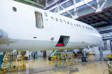 White passenger airplane in the hangar. Aircraft under maintenance. Checking mechanical systems for flight operations