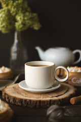 Still life with a cup of tea with milk, flowers and a teapot in the background