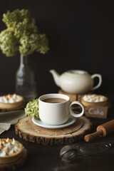 Still life with a cup of tea with milk, flowers and a teapot in the background