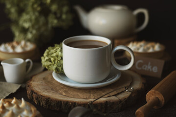 Still life with a cup of tea with milk, flowers and a teapot in the background