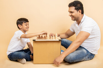 Happy young indian father play chess with his little son isolated over beige background. Indoor...