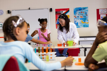 Happy diverse female teacher with schoolgirls doing experiments in lab