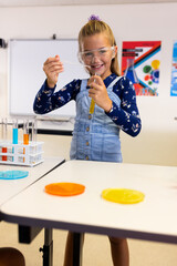 Portrait of happy caucasian schoolgirl with safety goggles doing experiment in lab
