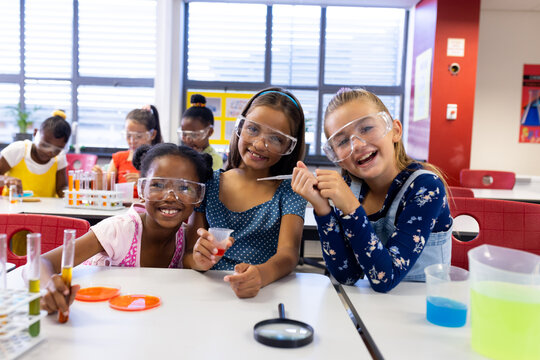 Portrait of happy diverse schoolgirls with chemistry items and liquids in elementary school class