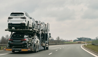 Car transporter carries new luxury vehicles along the motorway, back view of the trailer. Big car...