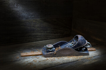 Small, vintage, rusty, iron Carpenter’s block hand-plane in profile on a strip of timber with shavings, soft, dark, mood lighting, copy space at top 