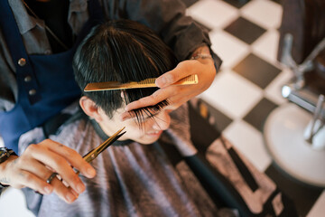 Handsome Asian man having a haircut at street hairdresser shop, professional street hair dresser - stylist cutting customer's hair by using electric hair trimmer and scissors.