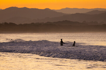 Fototapeta na wymiar Sunset view of surfers in silhouette along the Belongil Beach area in Byron Bay, New South Wales, Australia