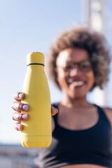 vertical photo with focus on the hand of a runner holding a yellow water bottle, concept of hydration in sports and active lifestyle, copy space for text