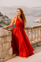 Woman red dress. Summer lifestyle of a happy woman posing near a fence with balusters over the sea.