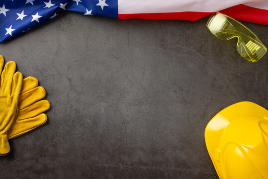 Honoring the contributions of construction workers on American Labor Day. Above shot of flag, helmet, gloves and safety glasses on grunge textured grey concrete. Suitable for ads or text
