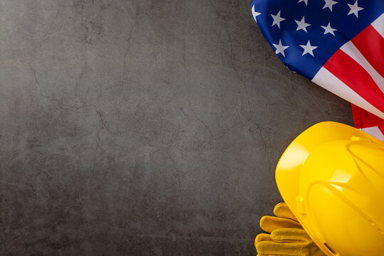 Celebrating the dedication of construction workers on Labor Day. Overhead view photo featuring american flag, helmet, gloves on grunge textured grey concrete background. Suitable for ads or text