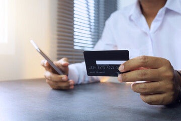 A man in a white shirt is using a credit card to shop online by making a transaction with a mobile phone or smartphone for convenience and shopping anywhere with global banking finance technology.