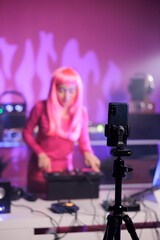 Cheerful artist performing electronic song at turntables while filming music process with phone camera in studio. Dj woman doing performance at nightclub with professional audio equipment