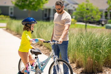Obraz premium Father and son in bike helmet for learning to ride bicycle at park. Father helping son cycling. Father and son on the bicycle on summer day. Little son trying to ride bike with father. Fathers day.