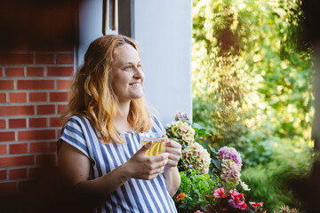 Contemplative pregnant woman holding herbal tea cup in balcony
