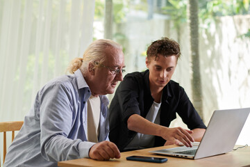 Senior man asking teenage grandson to help him with paying for online service