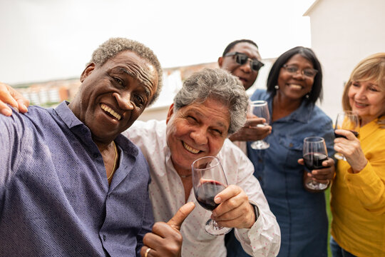 Happy senior man taking selfie with friends enjoying drinks in balcony - Powered by Adobe