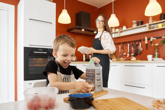 Happy boy grating cheese and preparing food with mother at home