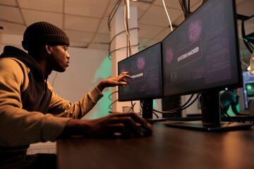 African american hacker planting trojan virus to steal data, looking at montors to create malware....