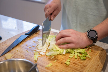 Hands of man chopping Chinese cabbage, preparing for fillings to make dumplings at home.