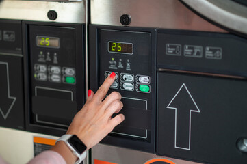 Young woman pressing button in washing machine at public laundry.