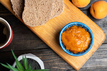 Apricot jam in a blue ceramic bowl, bread and fresh apricots on a wooden background