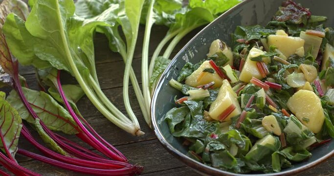 Blitva dish made with boiled potatoes, Swiss chard, garlic and olive oil. Fresh beet leaves on wooden rustic table. Table spin.
