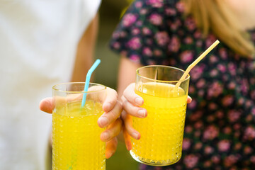 Trzymane w dłoniach szklanki ze słomką i sokiem pomarańczowym 