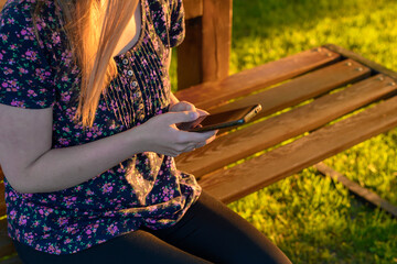 Kobieta siedzącą na ławce w parku korzystająca z telefonu komórkowego  - obrazy, fototapety, plakaty