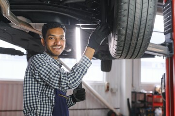 latin hispanic auto mechanic in uniform is examining a car while working in auto service