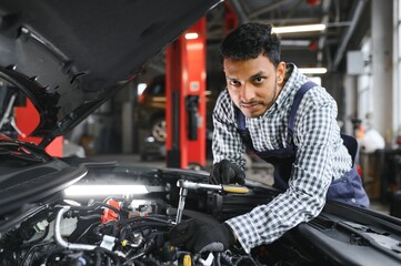 Fototapeta na wymiar latin hispanic auto mechanic in uniform is examining a car while working in auto service