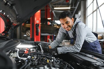 Plakat latin hispanic auto mechanic in uniform is examining a car while working in auto service