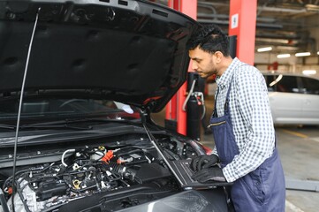 Fototapeta na wymiar Mechanic man mechanic manager worker using a laptop computer checking car in workshop at auto car repair service center. Engineer young man looking at inspection vehicle details under car hood.