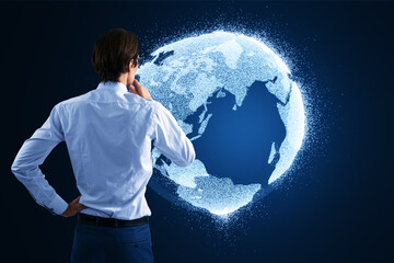 Back view of thoughtful young businnessman looking at glowing globe hologram on blurry blue background. Digital earth and metaverse concept.
