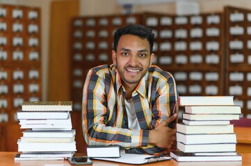 Male indian student at the library with book
