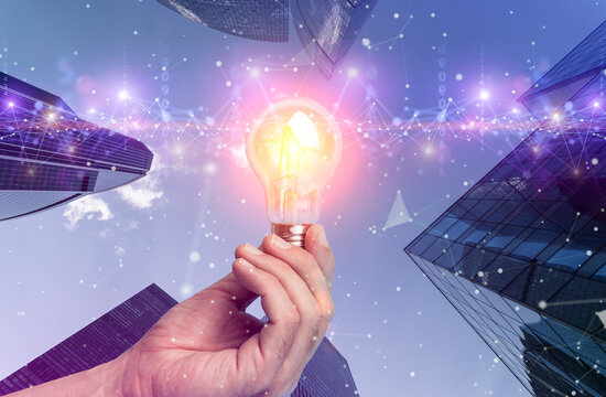 Business idea and financial solution. Light bulb in hand on the background of business skyscrapers. Economy, growth, income concept. - Powered by Adobe