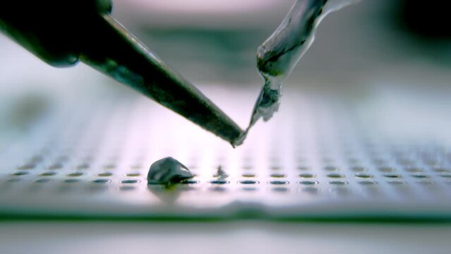 Drops of melted silver metal fall down on device panel under light. Soldering device melts metal from special stick with closeup